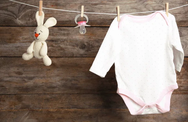 Bodysuit, chupeta e coelho de brinquedo na linha de lavanderia contra fundo de madeira. Acessórios para bebés — Fotografia de Stock