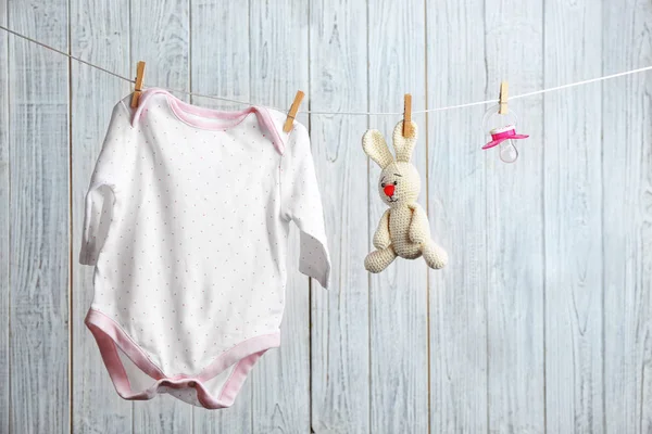 Bodysuit, chupeta e coelho de brinquedo na linha de lavanderia contra fundo de madeira. Acessórios para bebés — Fotografia de Stock