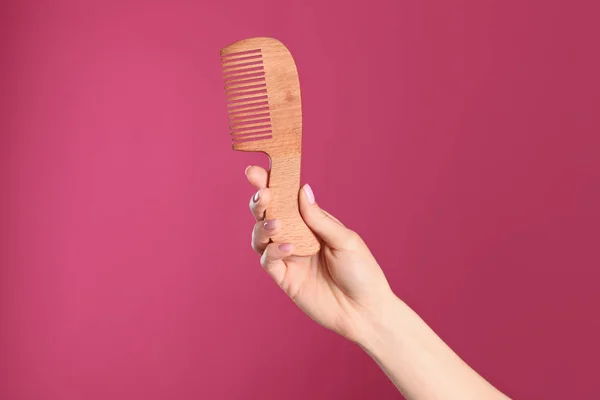 Woman holding wooden hair comb against crimson background, closeup. Space for text — Stock Photo, Image