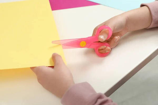 Child cutting color paper with plastic scissors at table, closeup — Stock Photo, Image