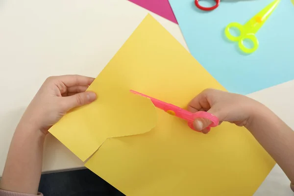 Child cutting color paper with plastic scissors at table, closeup — Stock Photo, Image