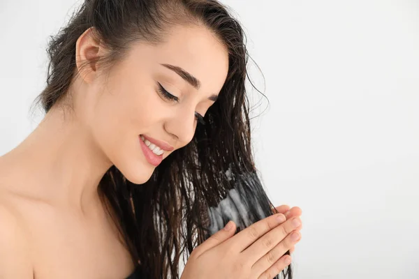 Hermosa mujer joven aplicando acondicionador de cabello sobre fondo blanco. Espacio para texto — Foto de Stock