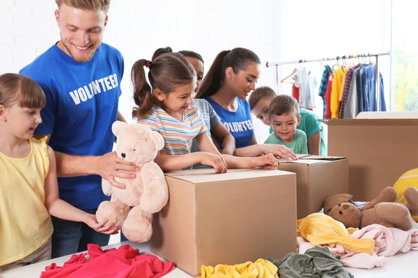 Vrijwilligers met kinderen die donatie goederen binnenshuis sorteren — Stockfoto