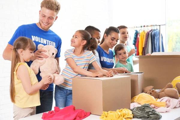 Voluntarios con niños clasificando bienes de donación en interiores — Foto de Stock