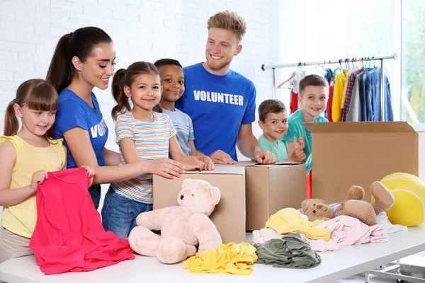 Voluntarios con niños clasificando bienes de donación en interiores — Foto de Stock