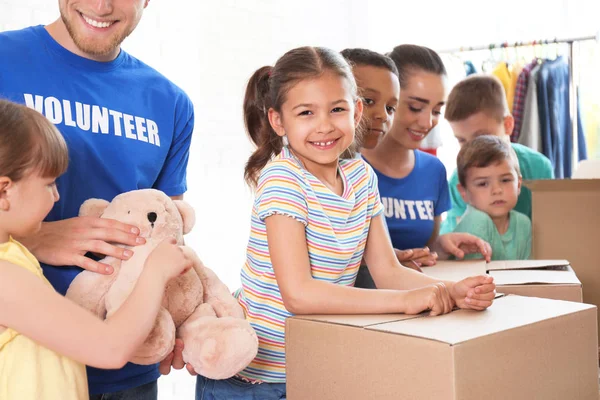 Voluntarios con niños clasificando bienes de donación en interiores — Foto de Stock