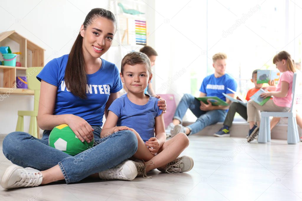 Young female volunteer with little boy sitting on floor indoors