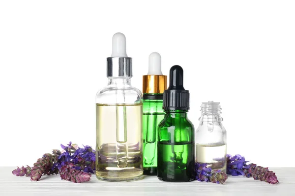 Flessen van salie etherische olie en bloemen op houten tafel, witte achtergrond — Stockfoto