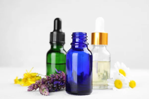 Butelki z różnych olejków eterycznych i kwiaty na jasnym stole — Zdjęcie stockowe