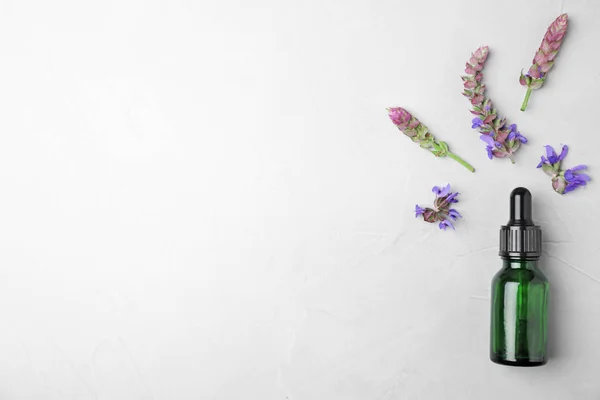 Butelka szałwii olejku i kwiatów na jasnym stole, płaski lay. Miejsce na tekst — Zdjęcie stockowe
