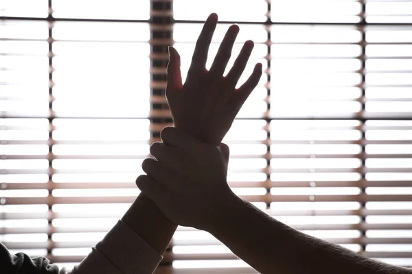 Man grijpen vrouw hand in de buurt van venster, close-up. Stop seksueel geweld — Stockfoto