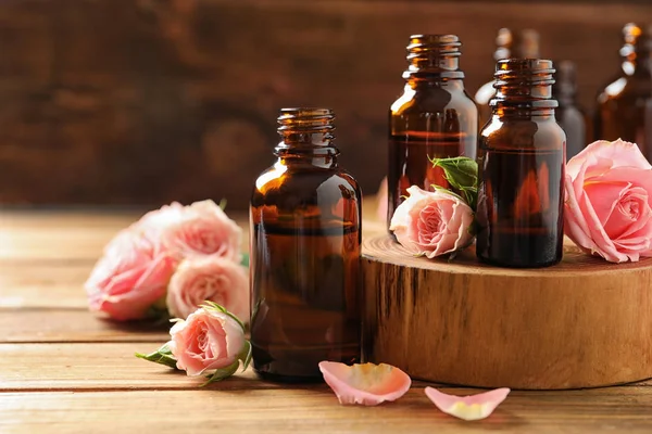 Bottiglie di olio essenziale di rosa e fiori freschi sul tavolo di legno, spazio per il testo — Foto Stock