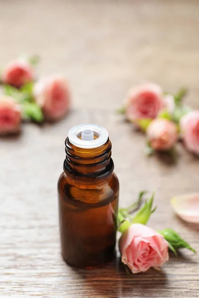 Fles Rose etherische olie en verse bloemen op houten tafel, ruimte voor tekst — Stockfoto