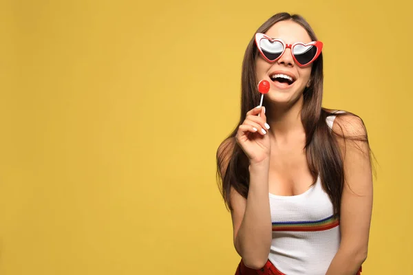 Portret van mooie jonge vrouw met hartvormige zonnebril en Lollipop op kleur achtergrond. Ruimte voor tekst — Stockfoto