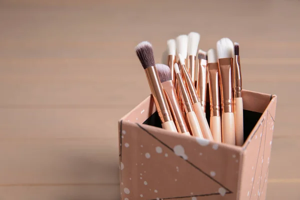 Organizer with professional makeup brushes on wooden table. Space for text