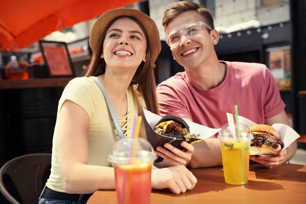 年轻的幸福夫妇与汉堡在街头咖啡馆 — 图库照片