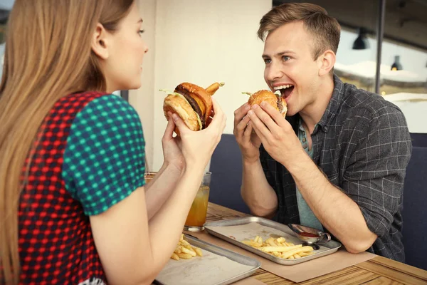 Young couple eating burgers in street cafe