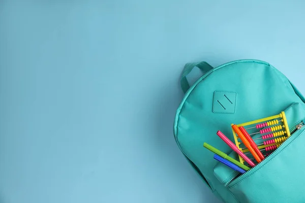 Стильний рюкзак з різним шкільним стаціонарним на світло-блакитному тлі, вид зверху. Простір для тексту — стокове фото
