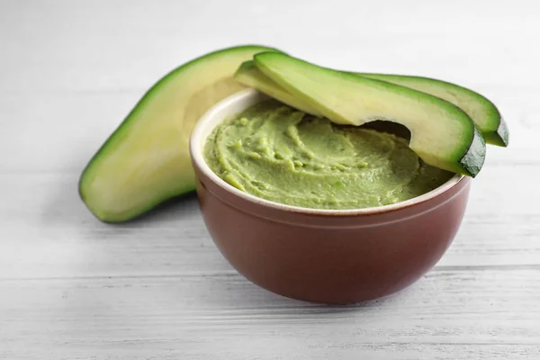 Bowl with guacamole sauce and ripe avocados on white wooden table — Stock Photo, Image