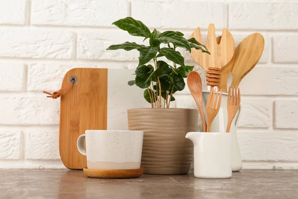 Potted plant and set of kitchenware on grey table near white brick wall. Modern interior design — Stock Photo, Image