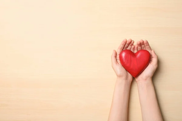 Mujer sosteniendo el corazón sobre fondo de madera, vista superior con espacio para el texto. Concepto de donación —  Fotos de Stock