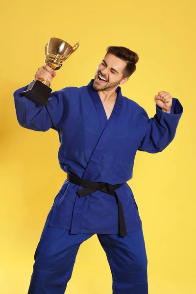 Портрет счастливого молодого человека в синем кимоно с золотым кубком на желтом фоне — стоковое фото