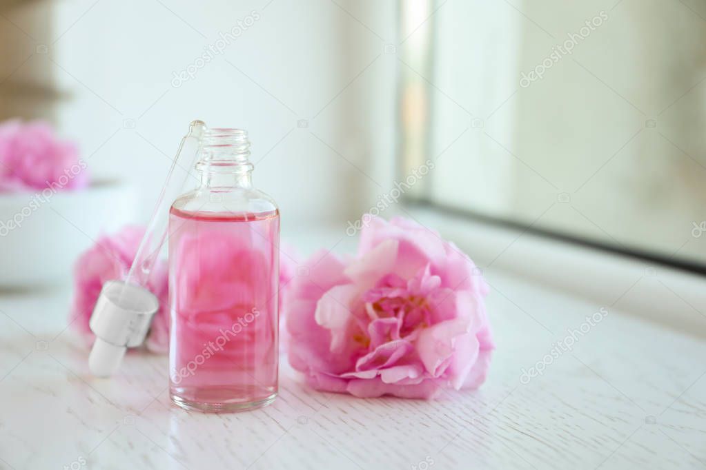 Bottle of rose essential oil, pipette and fresh flowers on window sill, space for text