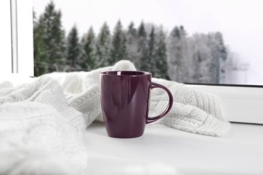 Sıcak kış içkisi ve karlı orman manzaralı pencere yakınında sıcak eşarp