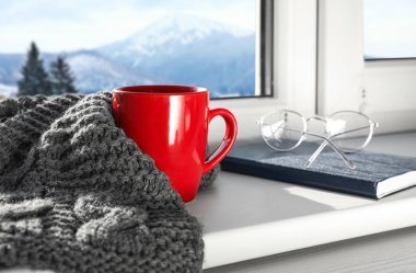 Sıcak kış içeceği, atkı, gözlük ve dağ manzara manzaralı pencere yakınında kitap
