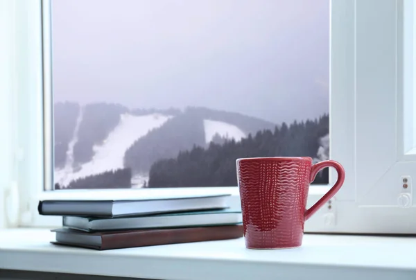 Warme drank en boeken in de buurt van het raam met uitzicht op de Winterberg landschap — Stockfoto