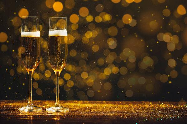 Glasses of champagne and golden glitter on table against blurred background, space for text. Bokeh effect