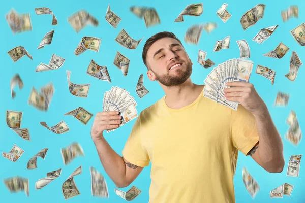 Happy young man with dollars under money rain on blue background — Stock Photo, Image