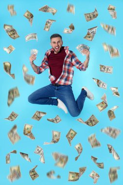 Dolar mavi arka plan üzerinde para yağmur altında atlama ile Mutlu genç adam