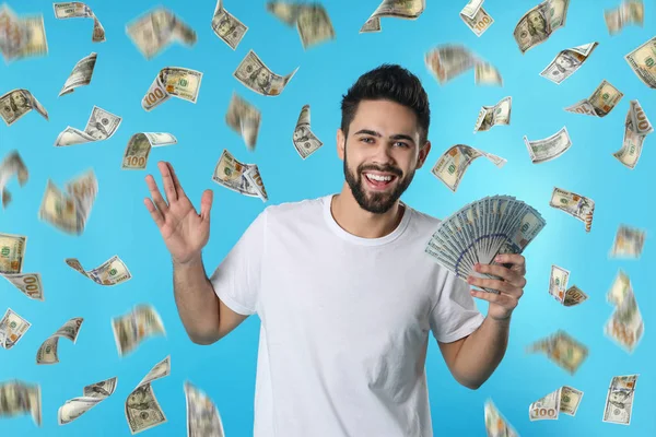 Happy young man with dollars under money rain on blue background — Stock Photo, Image