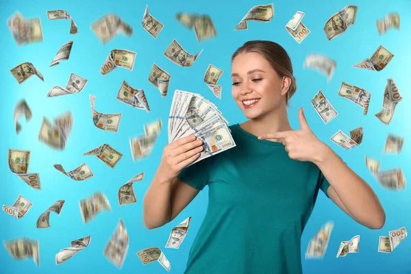 Mujer joven feliz con dólares bajo la lluvia de dinero sobre fondo azul — Foto de Stock