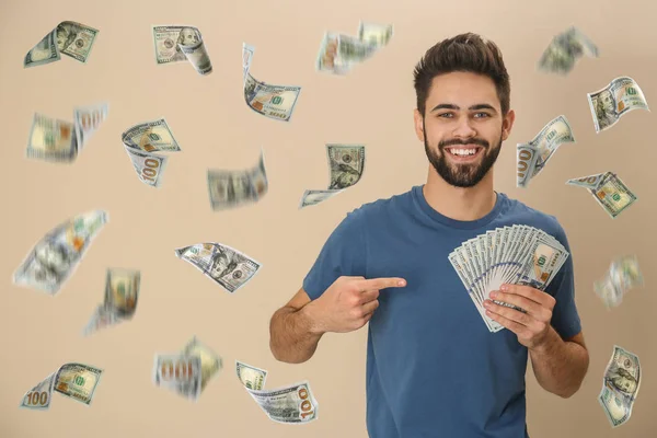 Glücklicher junger Mann mit Dollars unter Geldregen auf beigem Hintergrund — Stockfoto