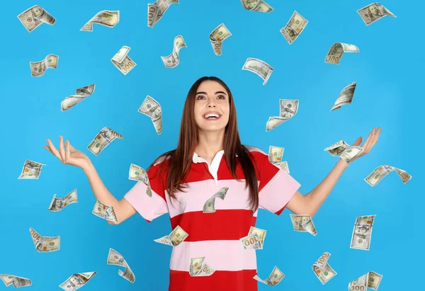 Happy young woman under money rain on blue background