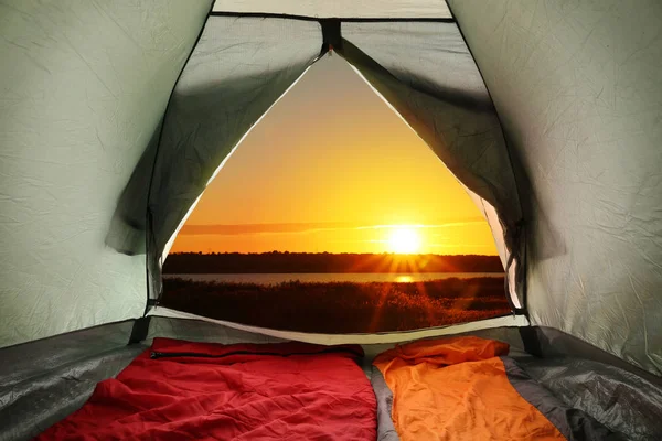 Tente de camping avec sacs de couchage près de la rivière au coucher du soleil, vue de l'intérieur — Photo