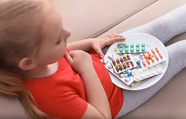 Litet barn med tallrik med olika piller hemma. Hushållens fara — Stockfoto