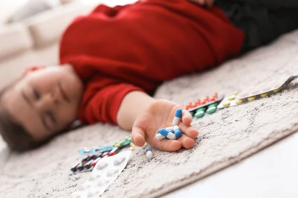 Маленький бессознательный ребенок с таблетками, лежащими на полу дома. Опасность для семьи — стоковое фото
