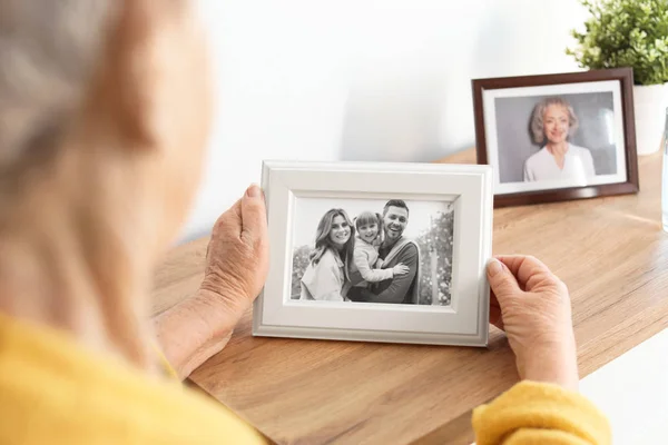 Elderly woman with framed family portrait at home