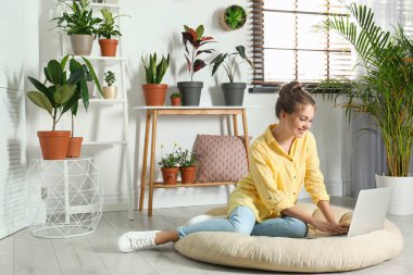 Farklı ev bitkileri ile odada dizüstü bilgisayar kullanan genç kadın