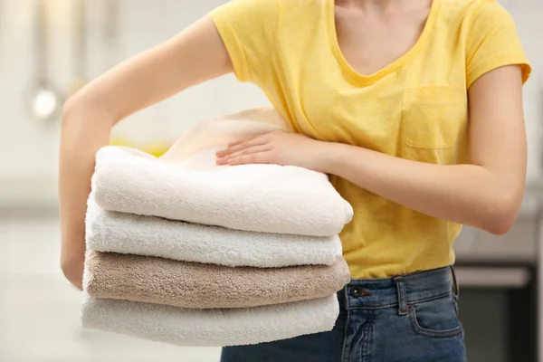 Mulher segurando toalhas limpas dobradas na cozinha, close-up. Dia de lavandaria — Fotografia de Stock