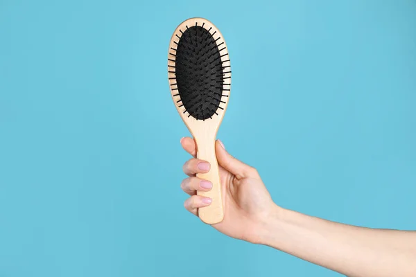 Woman holding wooden hair brush against blue background, closeup. Space for text