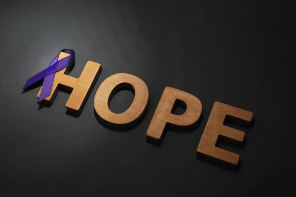 Lilla bevissthetsbånd og ord HOPE laget av trebokstaver på svart bakgrunn – stockfoto