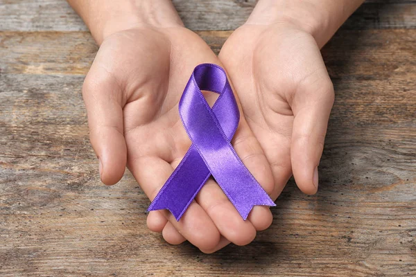 Man with purple awareness ribbon on wooden background, closeup