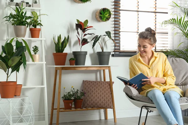Young woman reading book in room with different home plants