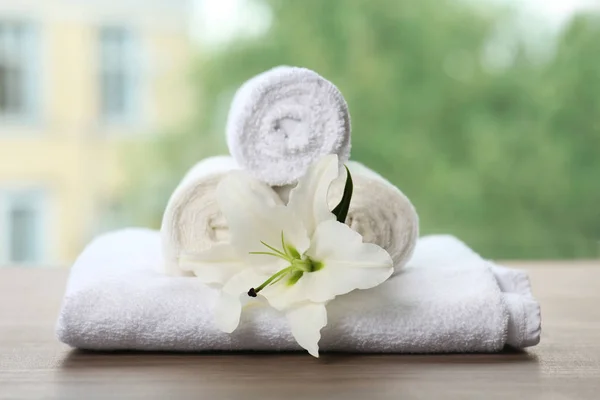 Stapel frischer Handtücher und Blumen auf dem Tisch vor verschwommenem Hintergrund — Stockfoto