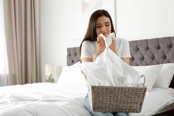 Young woman smelling fresh laundry in bedroom. Space for text — Stock Photo, Image