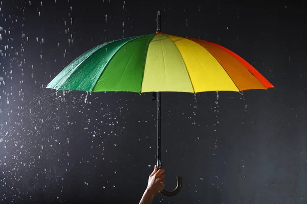 Жінка тримає яскраву парасольку під дощем на темному тлі, крупним планом — стокове фото